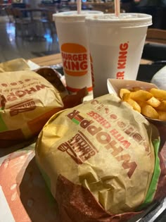 two burgers and fries are sitting on the table next to each other with drinks