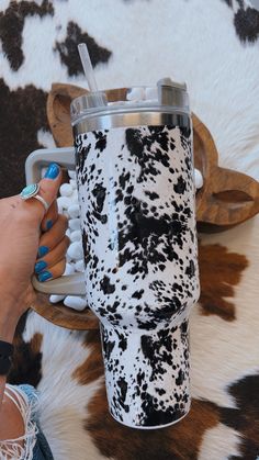 a woman is holding a cup in her hand while sitting on a cow print rug