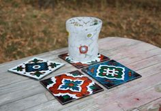 four coasters sitting on top of a wooden table in front of a white cup