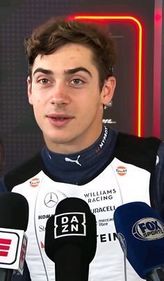 a young man is speaking into microphones in front of a neon sign