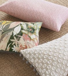 three pillows on the floor, one pink and one green with white flowers in them