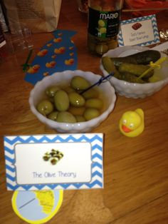 two bowls filled with green olives next to a yellow rubber ducky toy on a wooden table