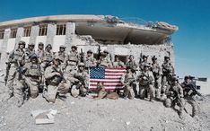 a group of soldiers posing in front of a building with an american flag on it