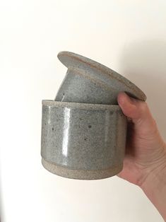 a hand is holding a gray cup in front of a white wall