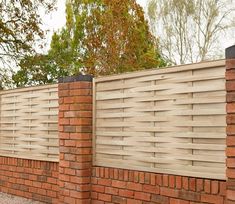 a brick wall with a wooden fence on the side and trees in the back ground