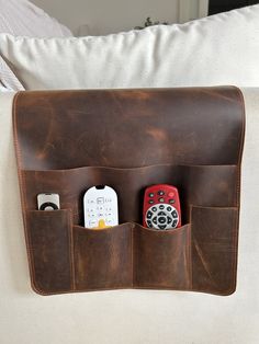 two cell phones are in the pocket of a brown leather case on a white couch