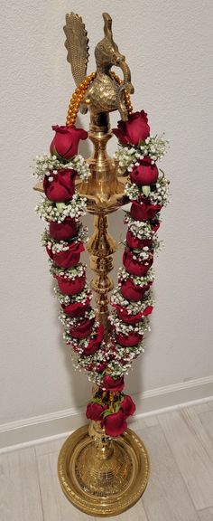 a golden vase with red roses and white baby's breath in it sitting on top of a gold pedestal