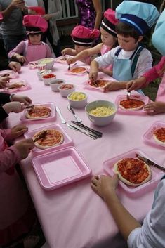 a group of children sitting at a table with pizzas on pink paper trays