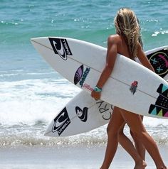 two women walking on the beach with their surfboards