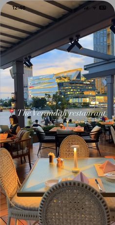 an outdoor dining area with tables and chairs overlooking the water at dusk in front of a cityscape