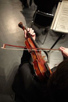 a person playing the violin in front of an orchestra conductor with his hands on the strings