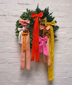 several different colored bows hang from a wreath on a white brick wall with greenery in the background