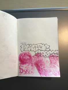 an open book with pink and white drawings on the pages, sitting on top of a table