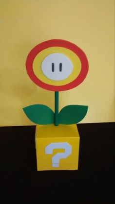 a paper flower in a box with question mark on it's side and yellow background