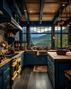 a large kitchen with blue cabinets and wooden flooring is pictured in this image, looking out onto the mountains