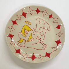 a plate with an angel on it sitting on a table next to a white wall