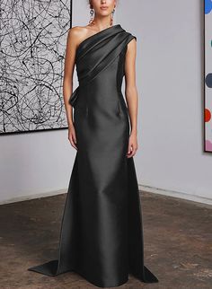 a woman standing in front of a painting wearing a black one - shoulder dress with an asymmetrical neckline