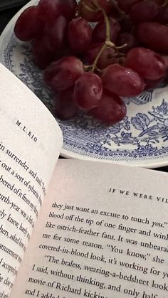 an open book with grapes on it and a plate full of grapes next to it