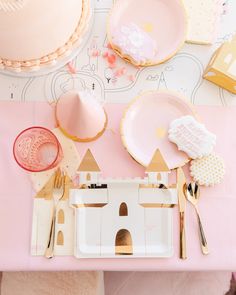 a pink table topped with plates and goldware next to a white castle shaped cake