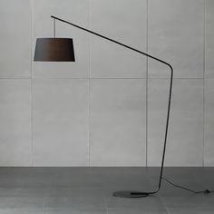 a floor lamp with a black shade on the base and a white wall behind it