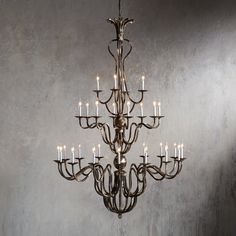 a chandelier with many lit candles hanging from it's arms and in front of a gray wall