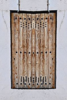 an old wooden door on the side of a white building with metal bars hanging from it's sides