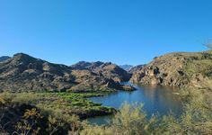 a lake surrounded by mountains and greenery on a sunny day with blue sky in the background