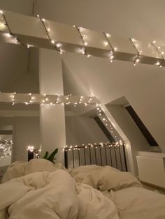 an unmade bed with white sheets and lights on the ceiling in a loft bedroom