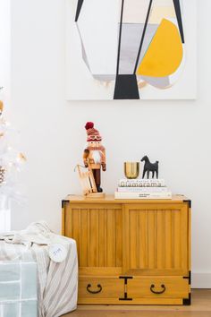 a small wooden chest sitting in front of a painting on the wall next to a christmas tree