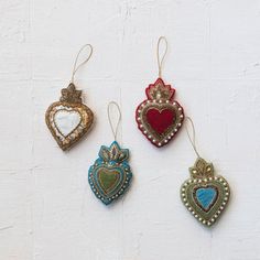 three ornaments are hanging from strings on a white wall, each with a heart shaped ornament