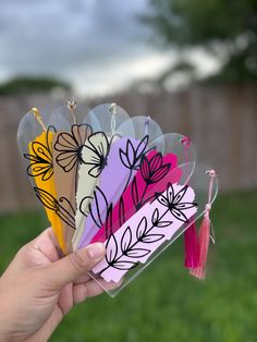 a person holding up four different colored flowers in their hand with a tassel on the end