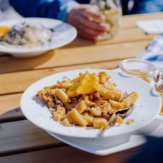 a white plate topped with pasta on top of a wooden table next to other plates