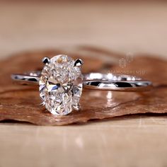 an oval cut diamond ring sitting on top of a wooden table next to a leaf