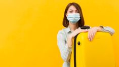 a woman wearing a face mask and holding a yellow suitcase with her hands on the handle