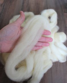 a hand is holding some white wool on a wooden table with it's thumb up