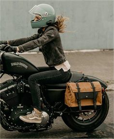 a woman riding on the back of a motorcycle down a street with a green helmet