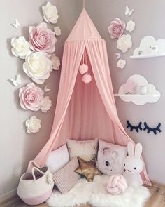 a pink canopy bed with flowers on the wall and stuffed animals in front of it