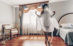 a woman in a white dress is dancing on the wooden floor near a bed and window