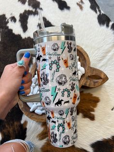 a woman is holding a travel mug in front of a cow print rug with her hand on the handle