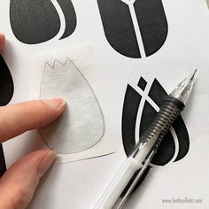 someone is cutting out some black and white paper with a pen on top of it