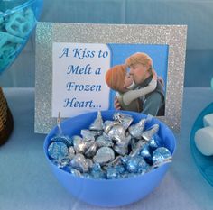 a blue bowl filled with chocolates next to a sign that says, a kiss to melt a frozen heart