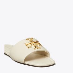 A single-band slide is made of soft leather and distinguished by our sculptural Eleanor hardware — redesigned with scaled-down dimension.Crafted in partnership with a Leather Working Group-certified tannery, supporting high standards in leather manufacturing and chemical management. White Tory Burch Sandals, Fashion Sandals Flat, Semi Annual Sale, Tory Burch Sandals, High Standards, Footwear Design Women, Designer Sandals, Sandal Fashion, Leather Working