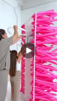 two women standing next to each other in front of a pink rack filled with plastic objects