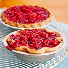 two pies sitting on top of a metal rack next to each other with cherries in them