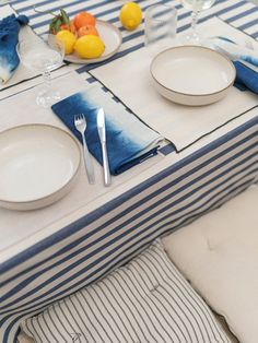 the table is set with blue and white striped linens, plates, silverware, and lemons