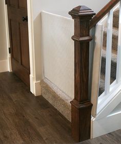 a wooden banister next to a white door and brown carpeted stair case in a home