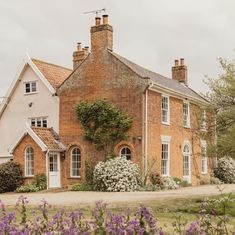 a large brick house with lots of windows and flowers in the foreground, on a cloudy day