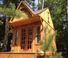 a small wooden house in the woods with pine trees around it's sides and windows