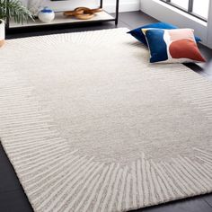 a white rug in a living room with pillows on the floor and a plant next to it