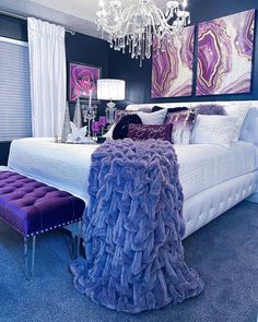 a bed with purple and white decor in a bedroom next to a chandelier